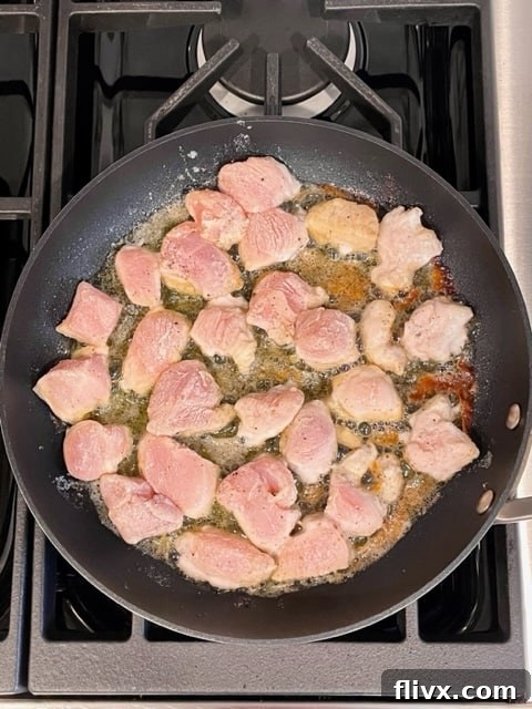 First step for Garlic Parsley Chicken: Chicken cubes are coated in a flour mixture and begin to sauté in a skillet, turning golden brown.