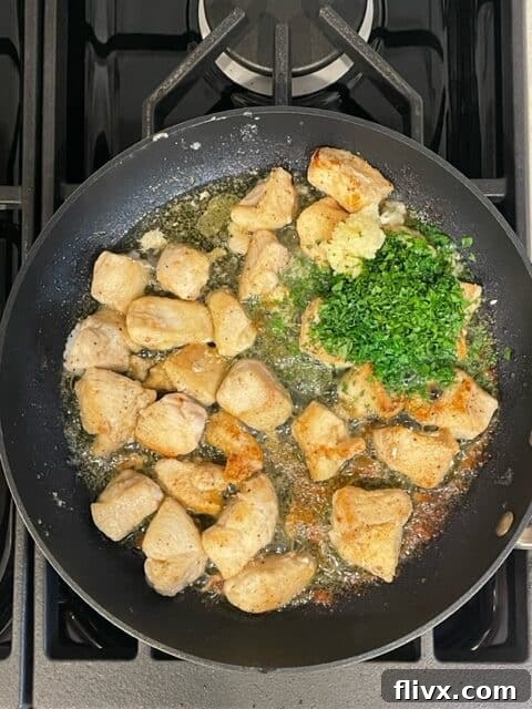 Third step for Garlic Parsley Chicken: Minced garlic, fresh parsley, and a knob of butter are added to the cooked chicken in the pan, ready to be tossed for coating.