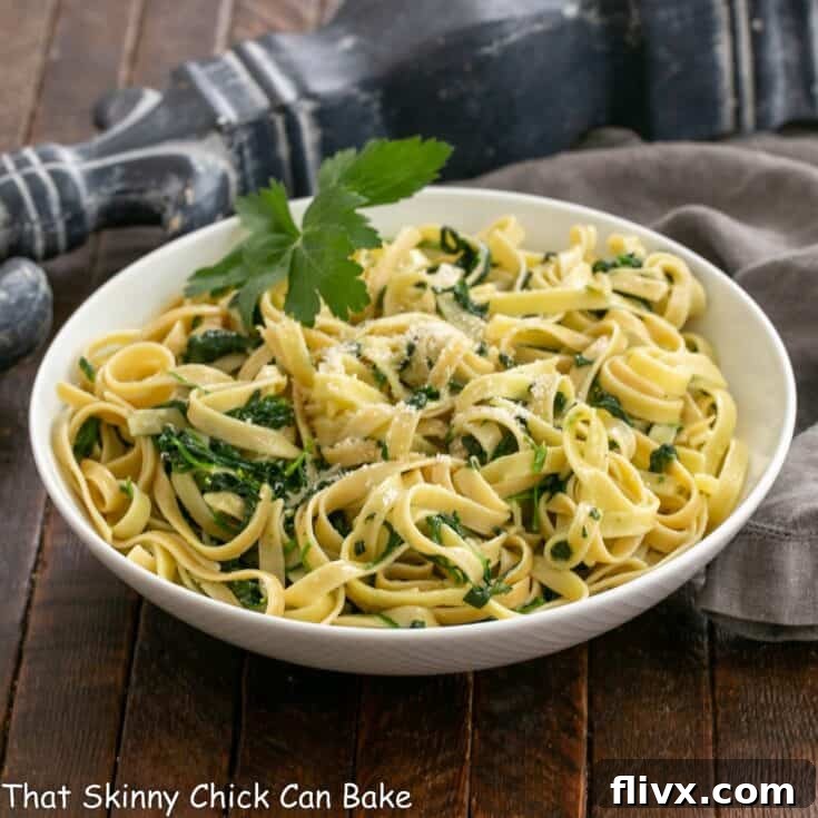 Bowl of fettuccine alfredo wih spinach in a white bowl with a parsley garnish.