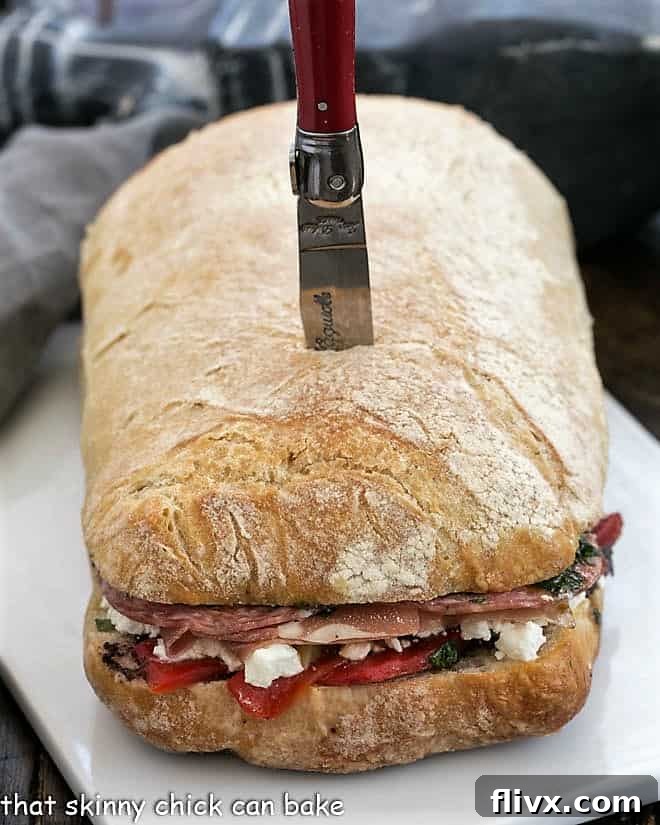 Picnic Sandwich before sliced on a ceramic tray, showcasing the full, pressed loaf with all its layers.