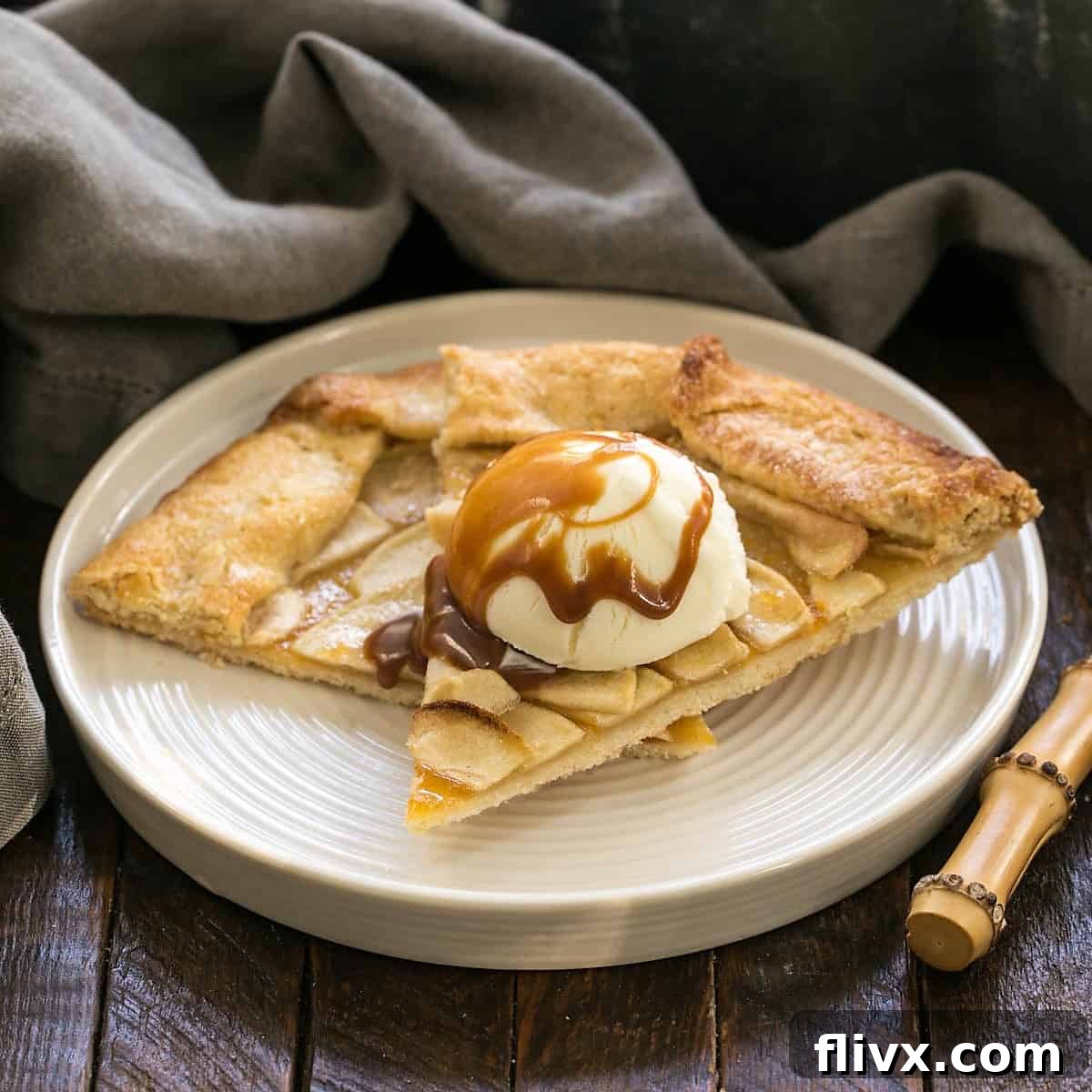 Two slices of apple crostata with a scoop of vanilla ice cream and a drizzle of caramel sauce, served on a white plate.