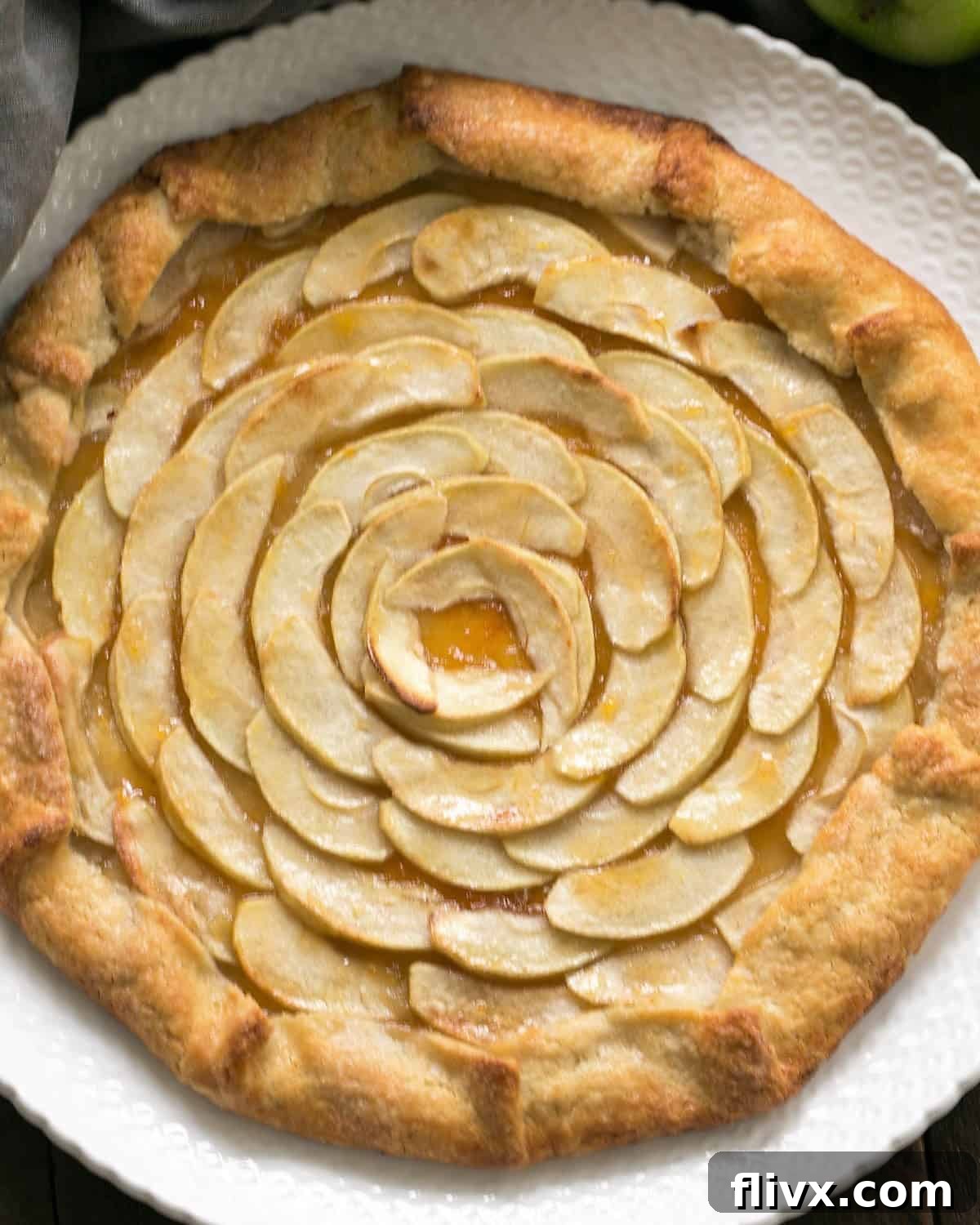 An overhead shot of a freshly baked Apple Crostata, golden brown and glistening, resting on a white serving plate.