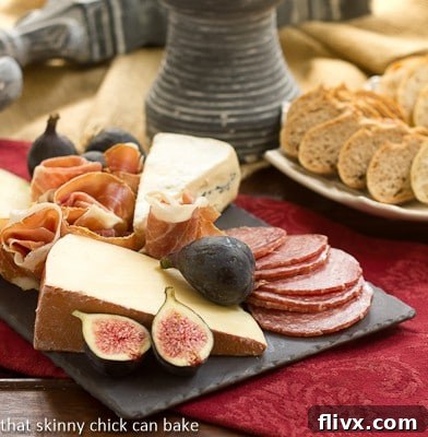 A slate cheese board topped with various meats, cheeses, grapes, and crackers, elegantly arranged on a red napkin.