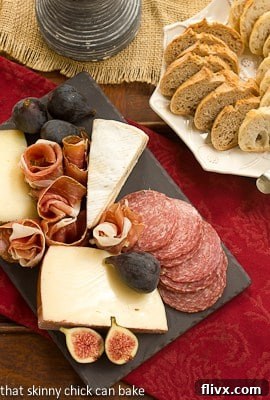 Overhead view of a gourmet meat and cheese tray next to a plate of fresh bread slices and a bowl of olives.