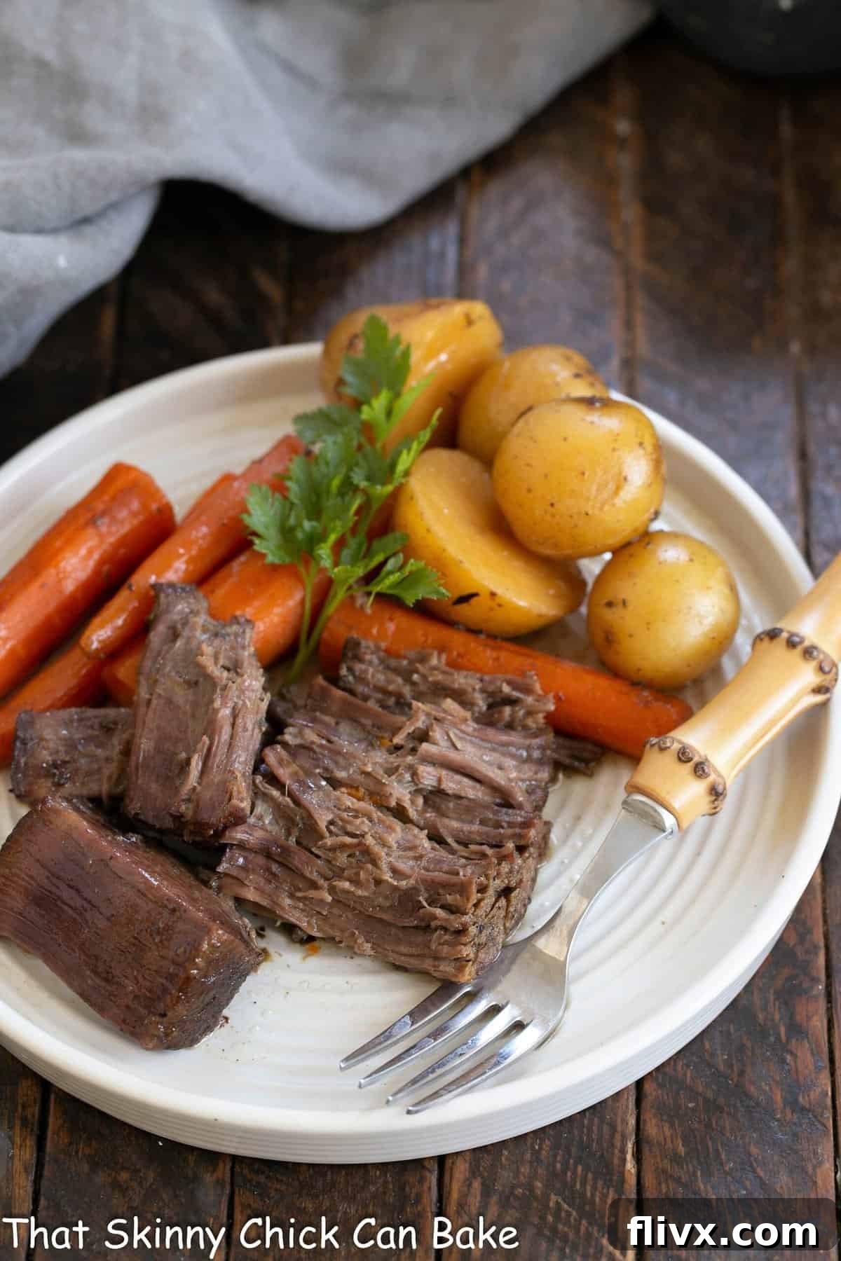 Beef pot roast on a white dinner plate with carrots potatoes and a bamboo handle fork.