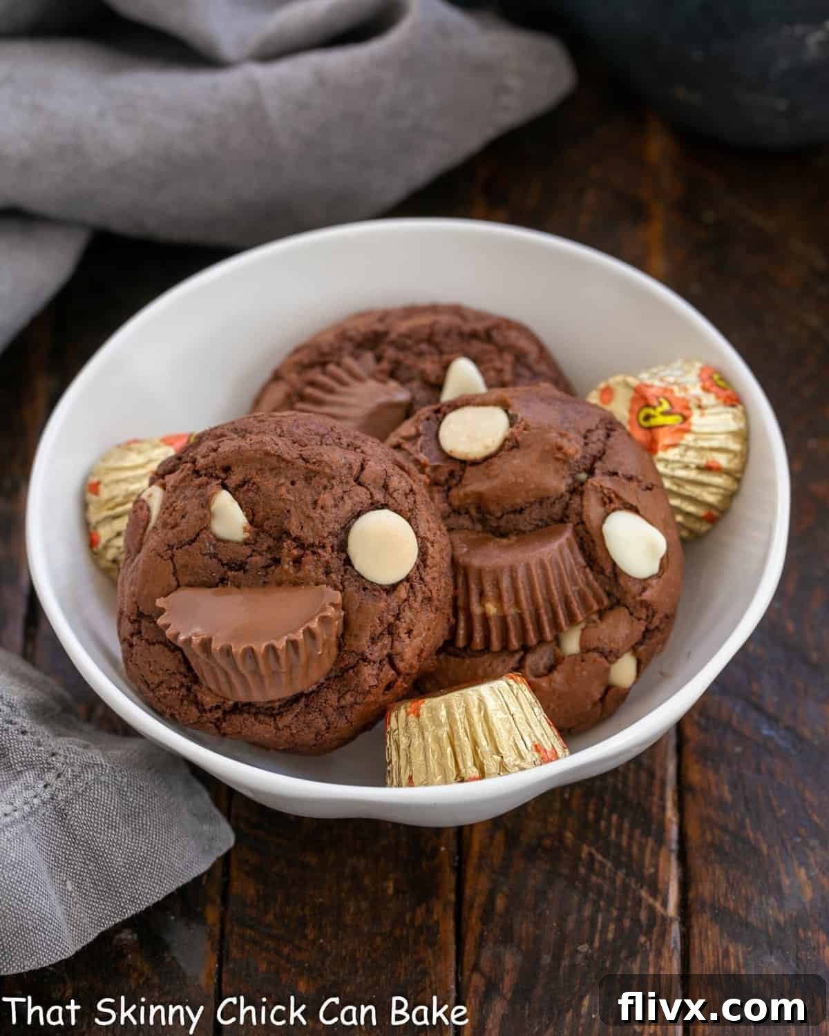 A white ceramic bowl holds several tempting Moose Tracks Cookies, showcasing their rich chocolate base, visible peanut butter cup halves, and glistening white chocolate chips, ready to be enjoyed.