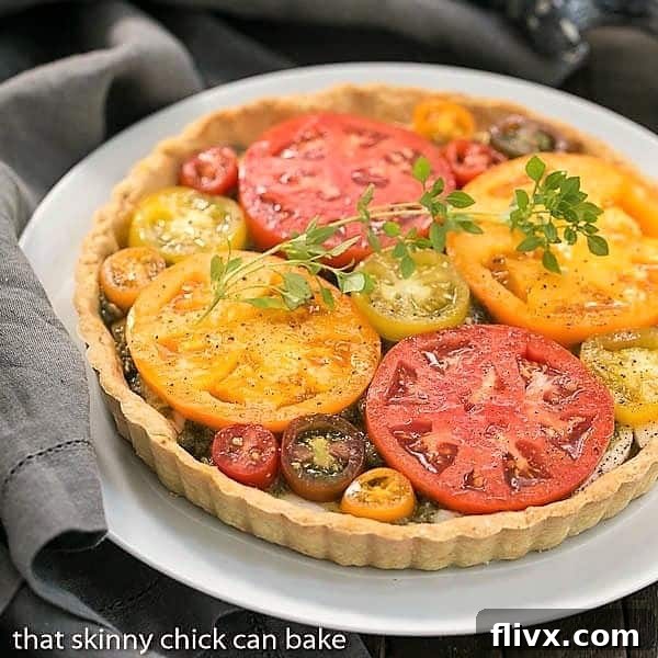 Fresh Tomato Tart on a white serving plate, garnished with fresh herbs, showcasing its vibrant colors and golden crust.