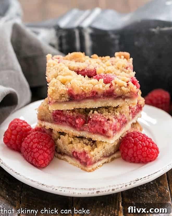 Streusel Topped Raspberry Squares stacked on a small plate with fresh raspberries and a sprig of mint.