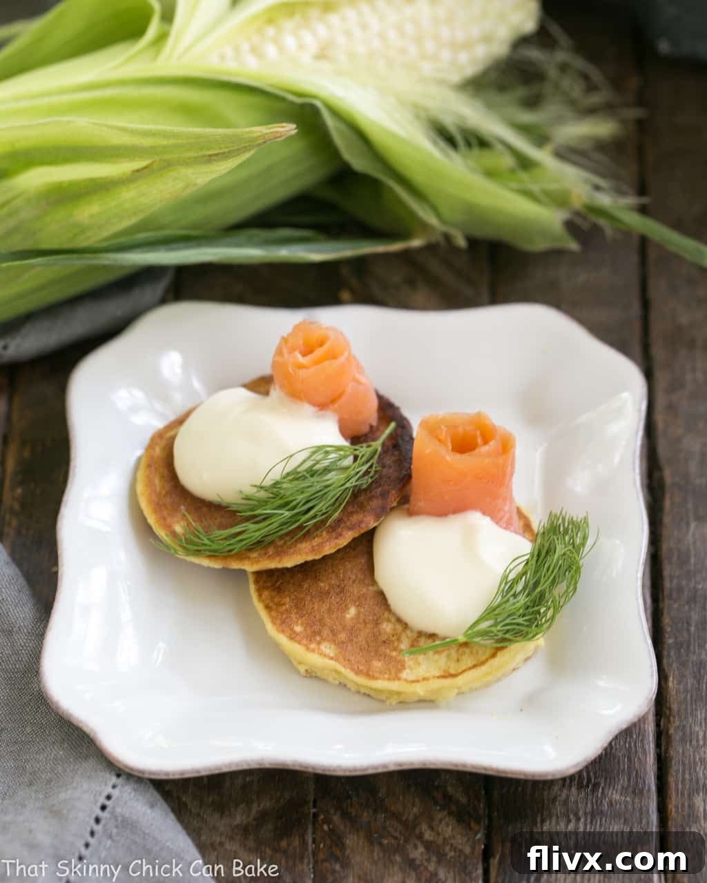 Fresh Corn Pancakes on a square plate topped with salmon and dill, ready to be served.