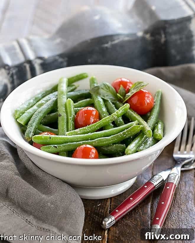Italian Sauteed Green Beans in a white ceramic bowl with two red handled forks, ready to serve.