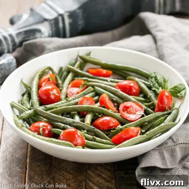 Haricot Verts with Grape Tomatoes in a white ceramic bowl with a garnish of fresh basil, close-up shot.