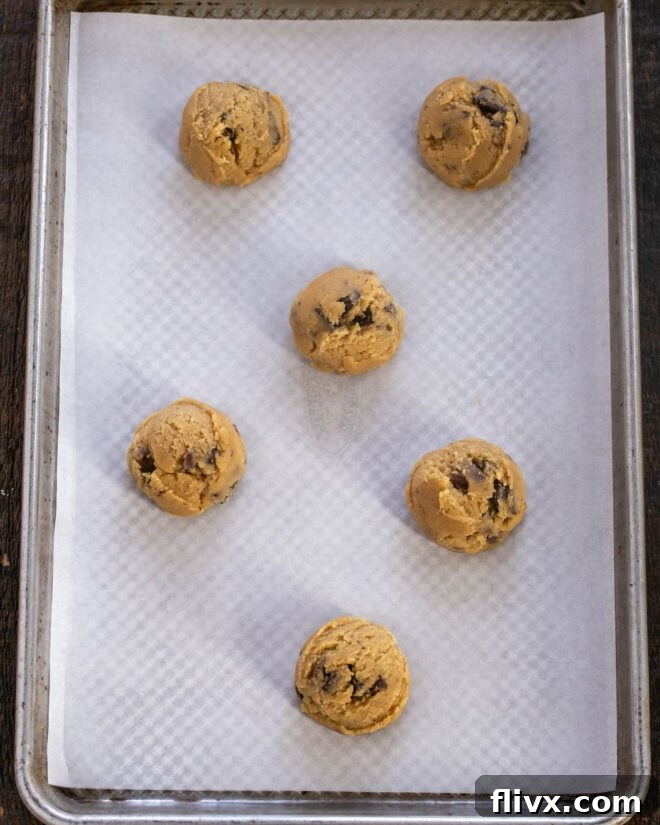 Scooped cookie dough balls placed two inches apart on a parchment-lined baking sheet, ready for baking.