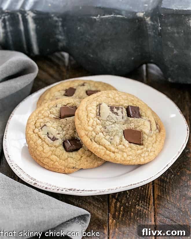 Three perfectly baked Ad Hoc Dark Brown Sugar Chocolate Chip Cookies, featuring melty chocolate chunks and a rich golden hue, artfully arranged on a round white plate.