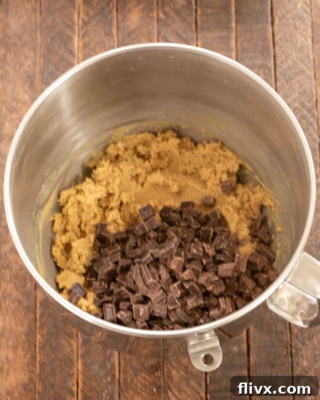 Dry ingredients (flour, baking soda, salt) being mixed into the wet ingredients, followed by the addition of chocolate chunks.