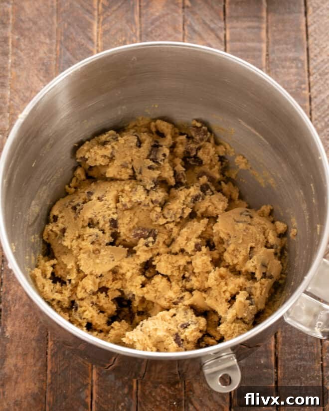Chocolate chunks being gently folded into the cookie dough until evenly distributed.