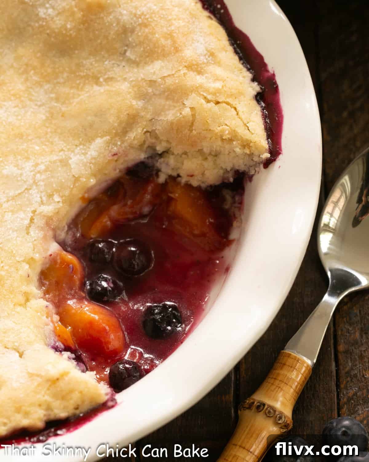 Close view of peach blueberry cobbler with a spoonful removed, revealing the delicious fruit filling and topping.