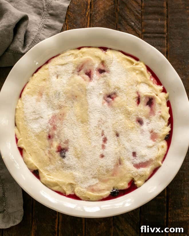 Spooning and spreading the batter evenly over the fruit filling.
