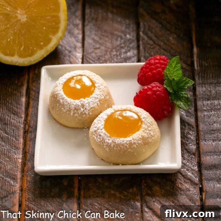 2 lemon thumbprint cookies on a small square white plate with fresh raspberries to garnish.
