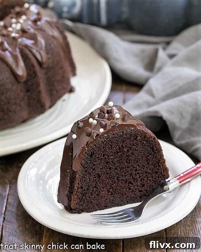 A perfectly sliced piece of moist Chocolate Sour Cream Bundt Cake with a rich ganache drizzle, served on a white plate with a red-handled fork.