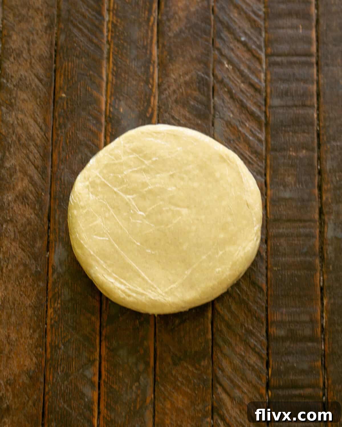 Step 2: The galette dough, after being mixed, is formed into a flat disc, wrapped tightly in plastic wrap, and placed in the refrigerator to chill.