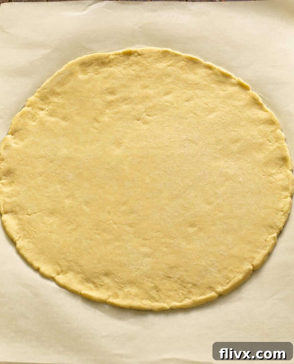 Step 3: Chilled galette dough being rolled out evenly into a large 12-inch round circle on a piece of parchment paper, ready for the peach filling.