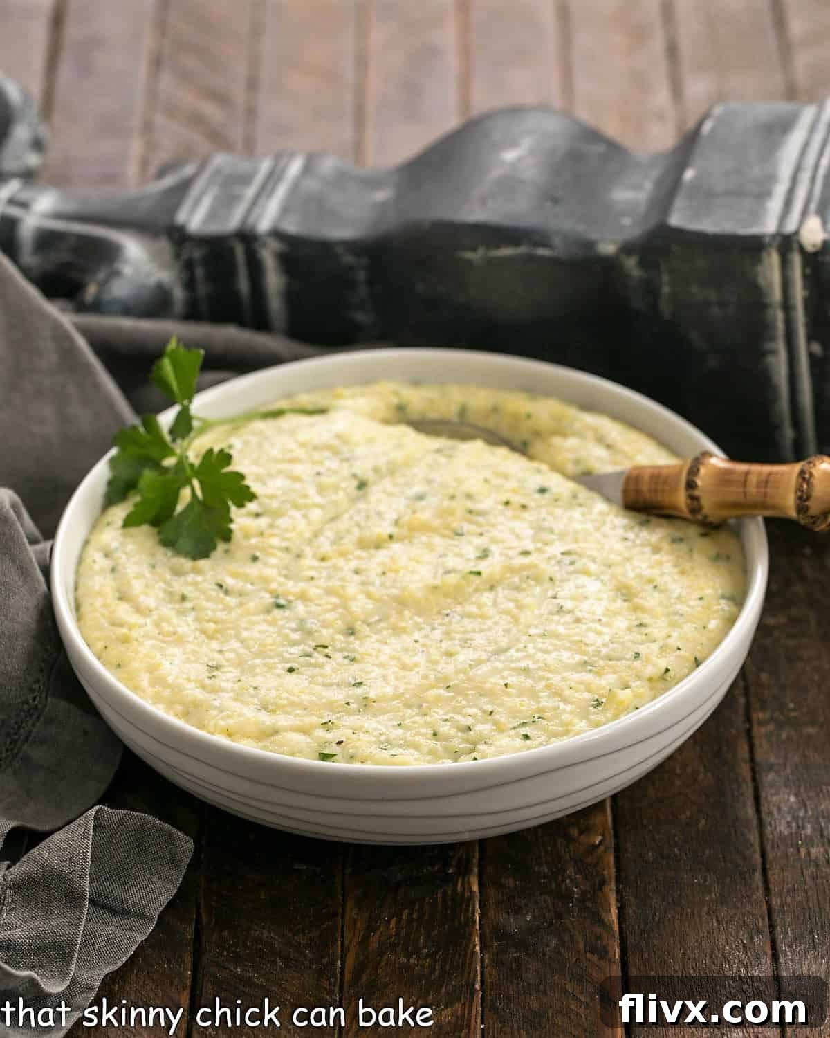 Easy Parmesan Polenta in a white bowl with a bamboo handle spoon garnished with parsley.