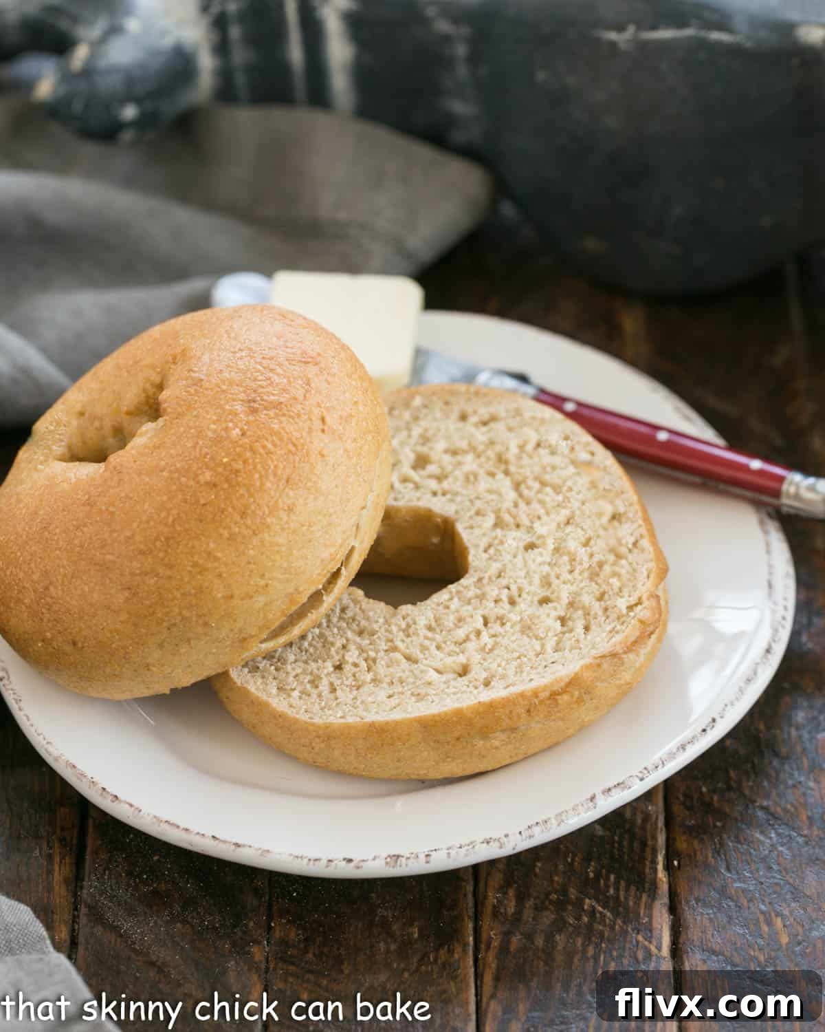 A freshly baked whole wheat bagel, perfectly sliced, rests on a simple white plate next to a red-handled knife, ready to be enjoyed.