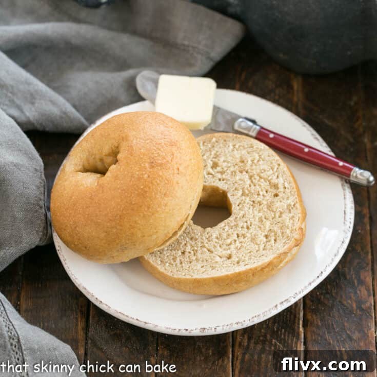 One Sliced whole wheat bagel on a white plate with a red handle knife topped with a pat of butter