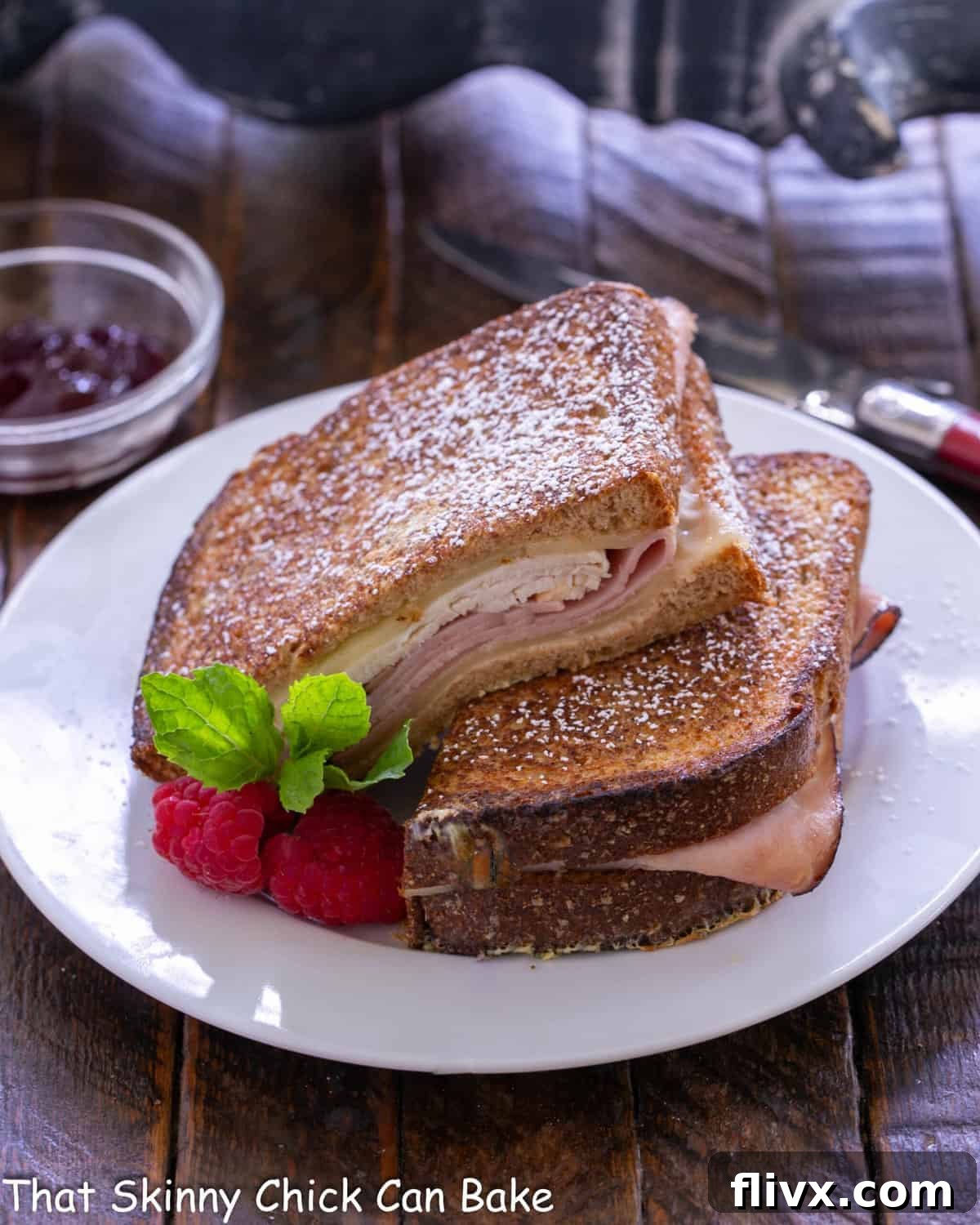Golden Brown Sweet and Savory Monte Cristo 2 Monte Cristo Sandwich on a white lunch plate, dusted with powdered sugar and served with jam.