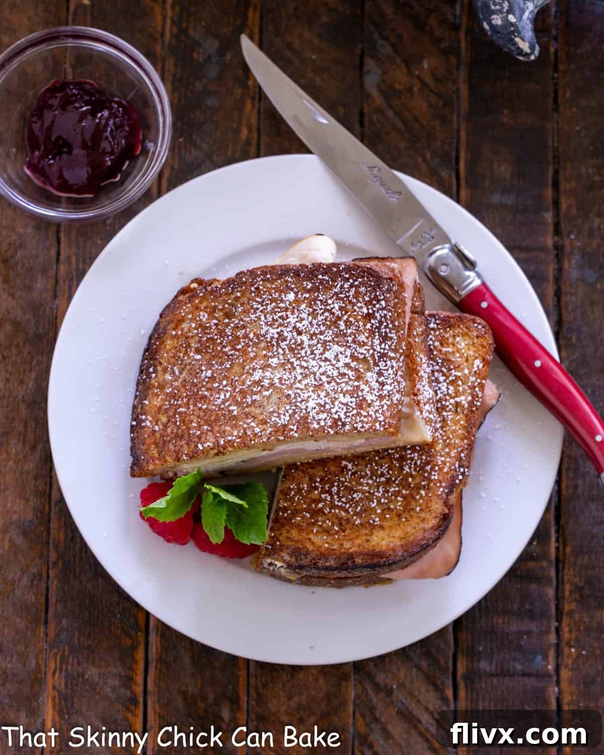 Golden Brown Sweet and Savory Monte Cristo 9 Overhead view of Monte Cristo Sandwich on a white plate with a red handled knife, dusted with powdered sugar.