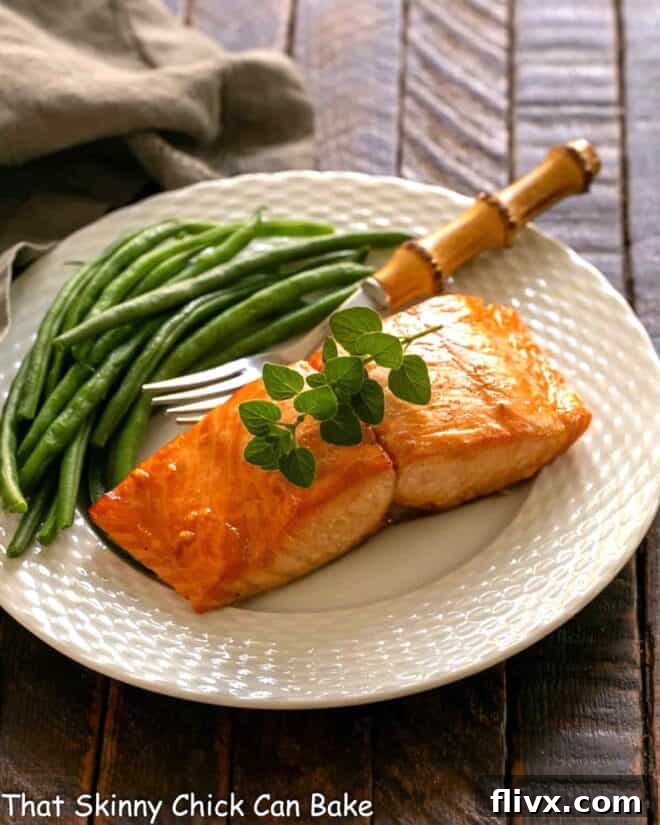 Date Night Grilled Salmon 2 Marinated salmon for two on a white plate with a fork and green beans, showcasing its golden, grilled perfection.
