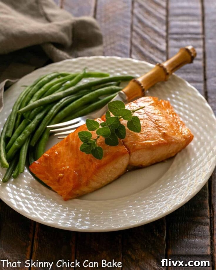 Marinated salmon for two on a white plate with a fork and green beans, beautifully plated for dinner.