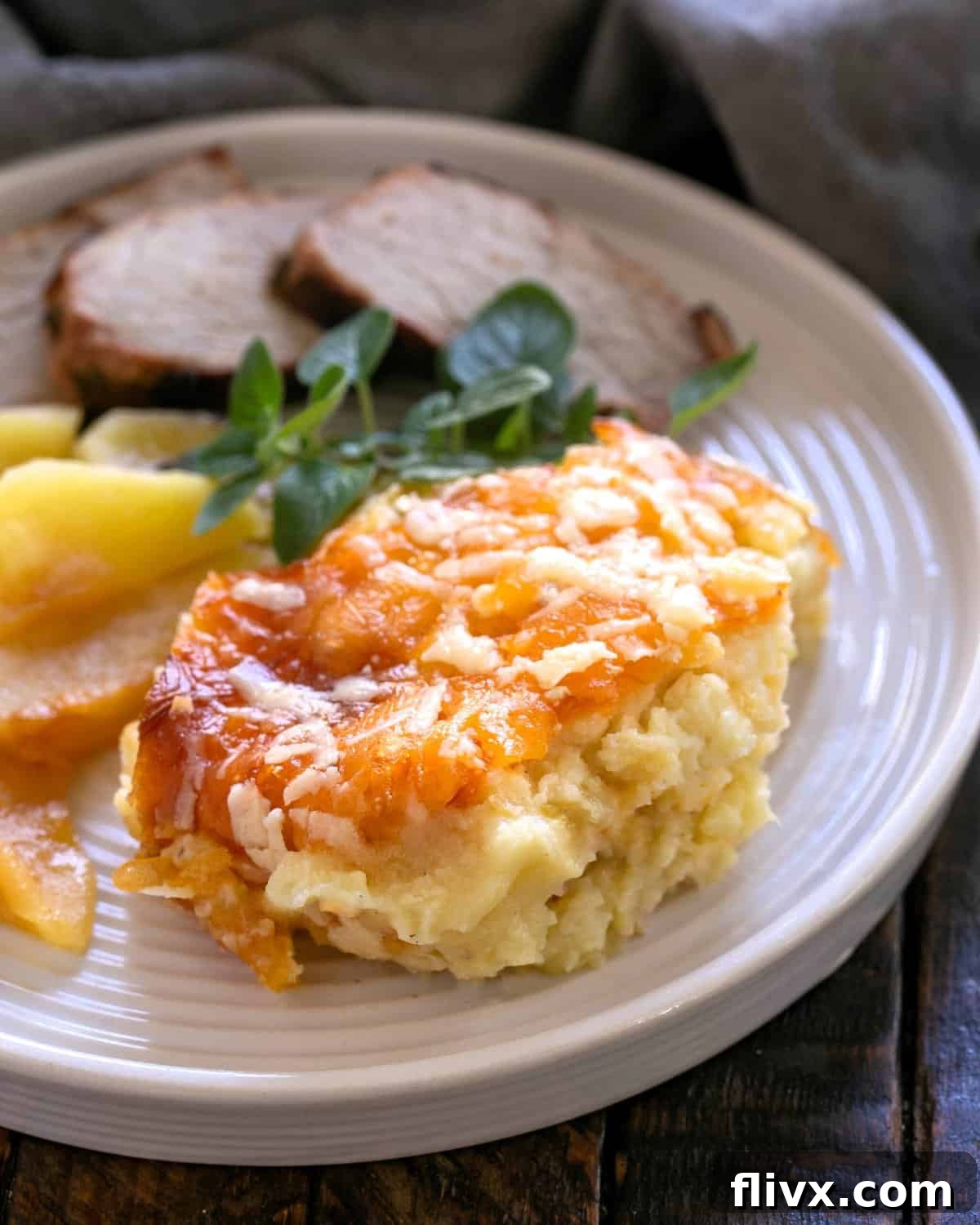 Serving of potato casserole on a white dinner plate with pork and apples.