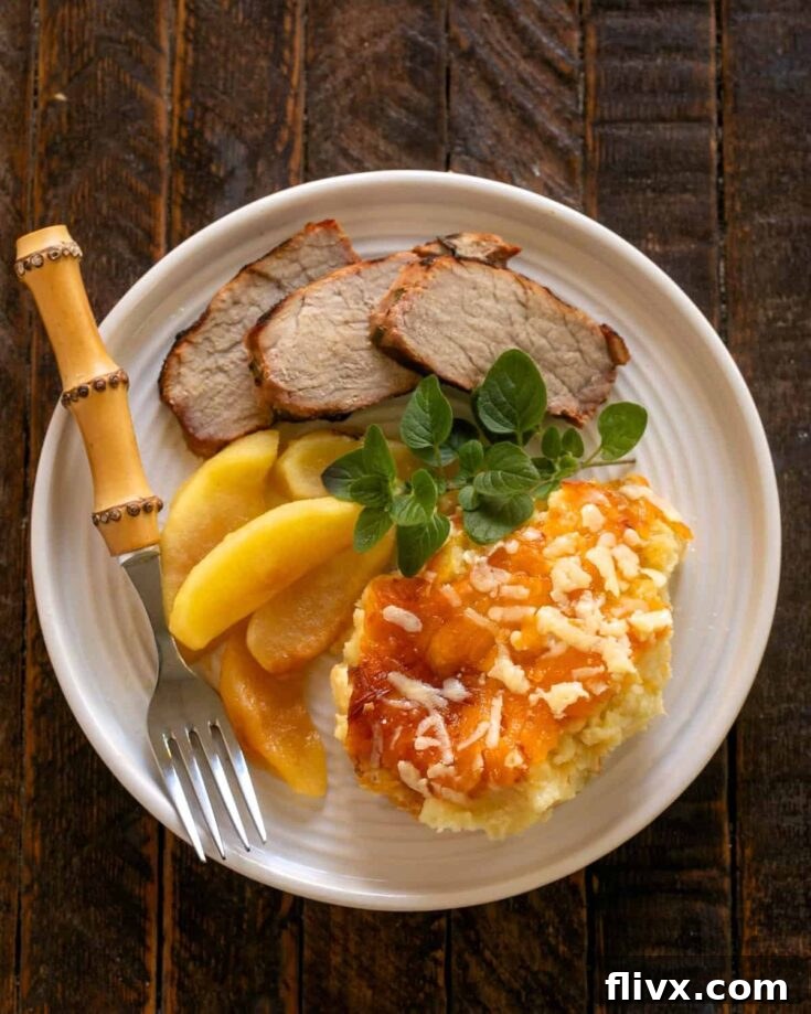 Overhead view of potato casserole, apples, pork slices with a fork on a white dinner plate.