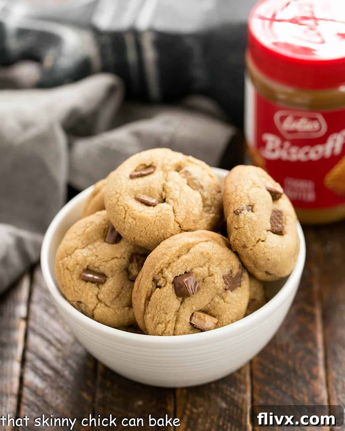 A beautifully arranged white bowl filled with golden-brown Toffee Biscoff cookies, with a jar of Biscoff cookie butter in the background, showcasing the key ingredient.