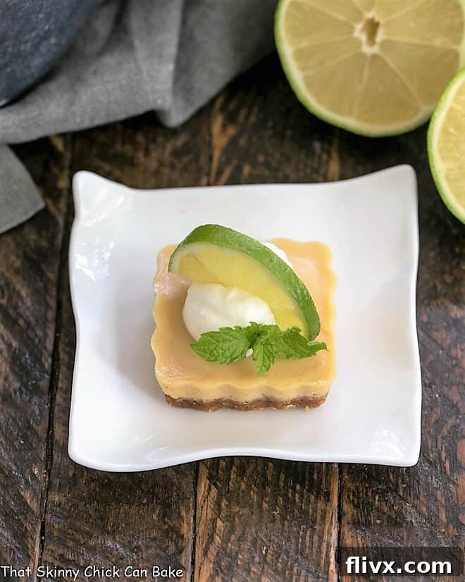 A single Key Lime Tartlet on a white plate, adorned with a swirl of whipped cream and a fresh lime slice.