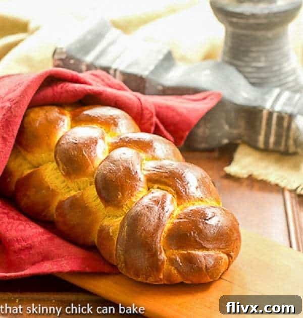 A beautifully braided Pumpkin Challah loaf wrapped in a festive red napkin, resting on a rustic cutting board, ready to be sliced.