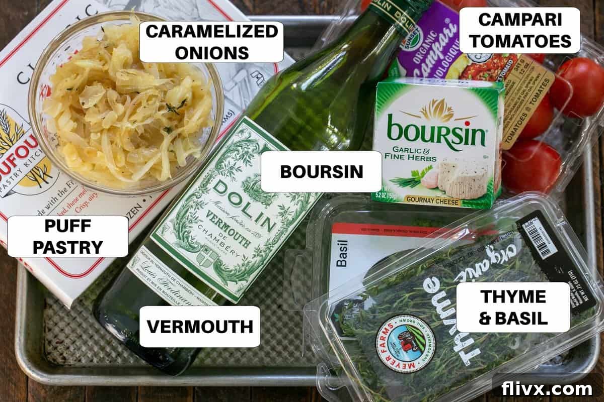 Fresh ingredients for Tomato Boursin Tarts laid out on a sheet pan, including puff pastry, Boursin cheese, tomatoes, and herbs.