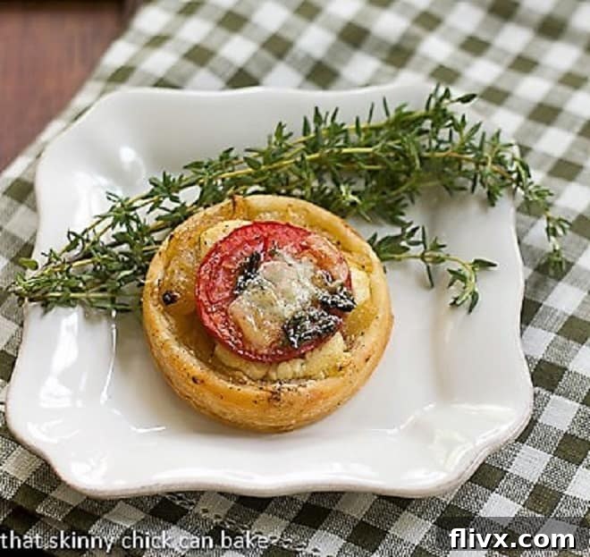 Single Tomato and Boursin Tartlet on a square white plate, garnished with a sprig of fresh thyme.