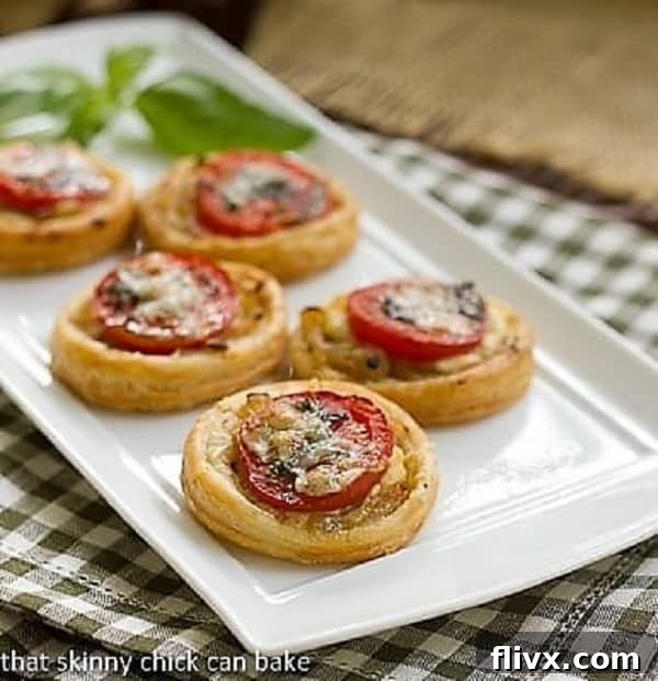 Tomato and Boursin Tartlets lined up on a white ceramic tray with a sprig of basil for garnish.