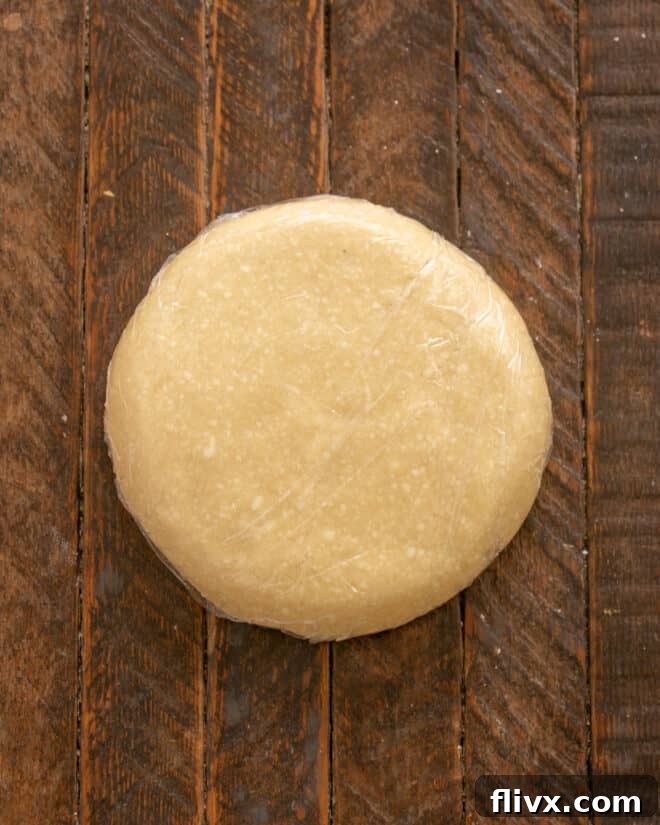 Step 5: The pie dough is divided into two halves, wrapped tightly in plastic wrap, and placed in the refrigerator to chill.