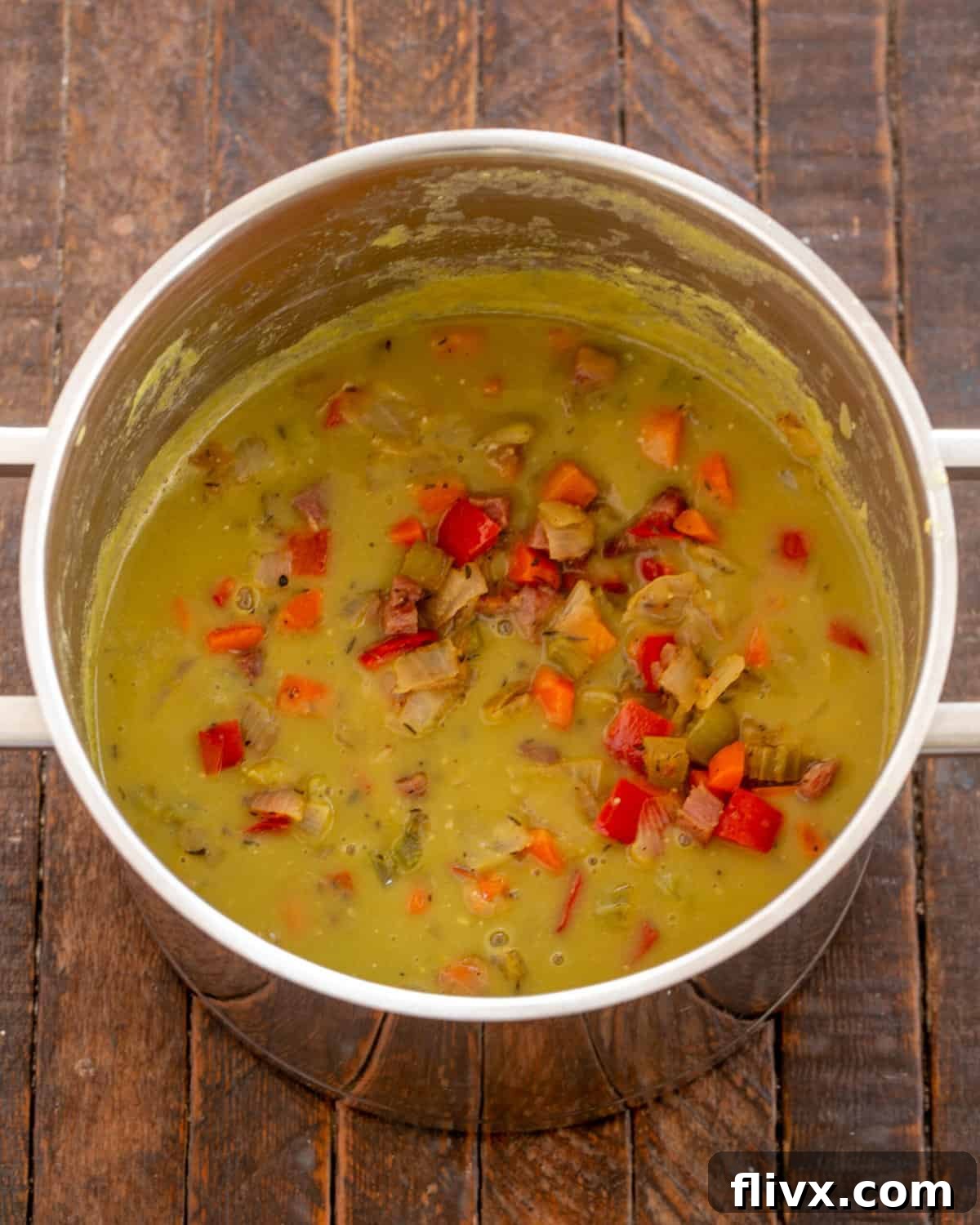 Adding sautéed vegetables, ham, and a ham bone to the pureed pea soup.