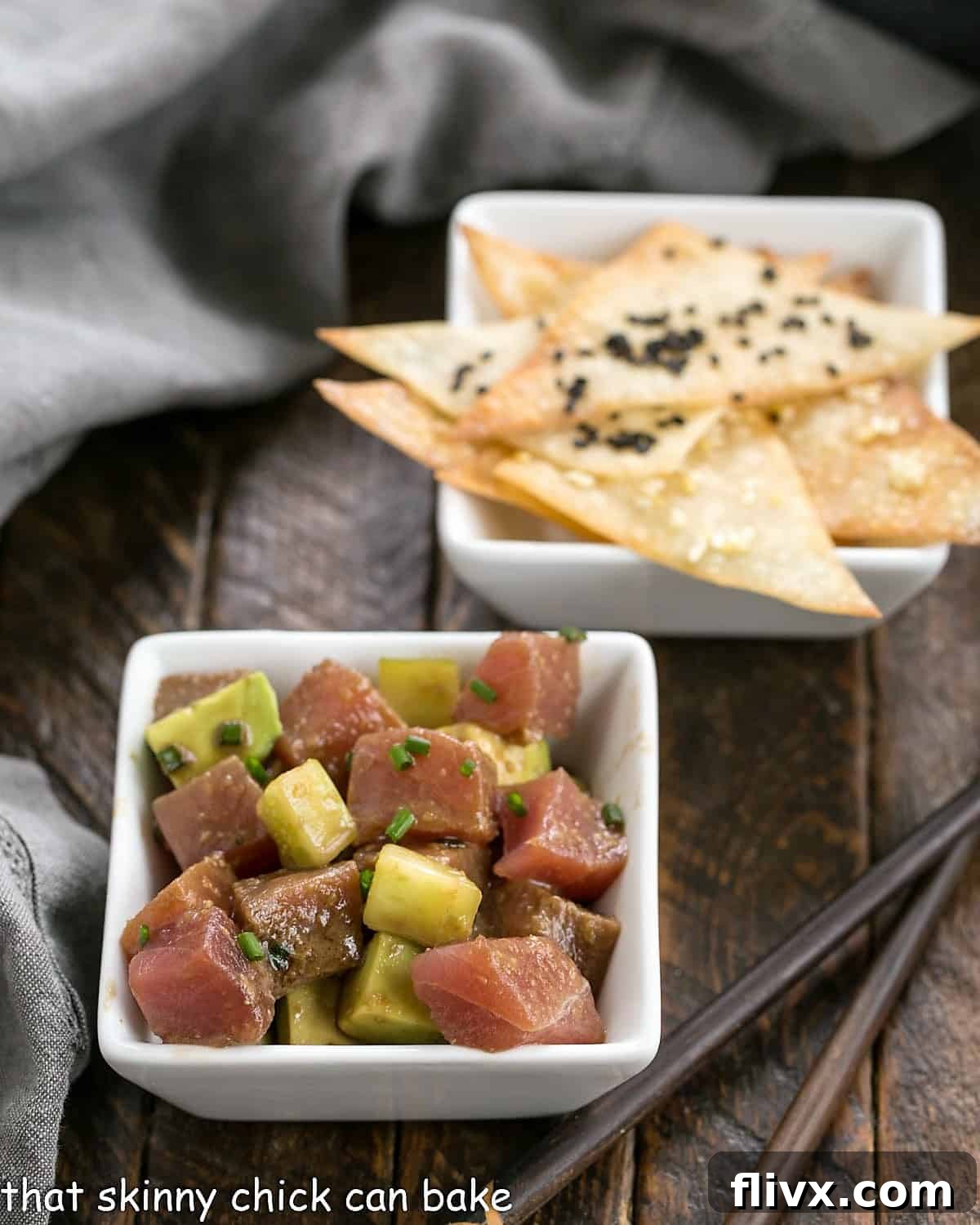 A square bowl filled with vibrant Tuna Tartare, garnished with fresh chives, placed in front of a small white bowl of golden-brown wonton crisps.