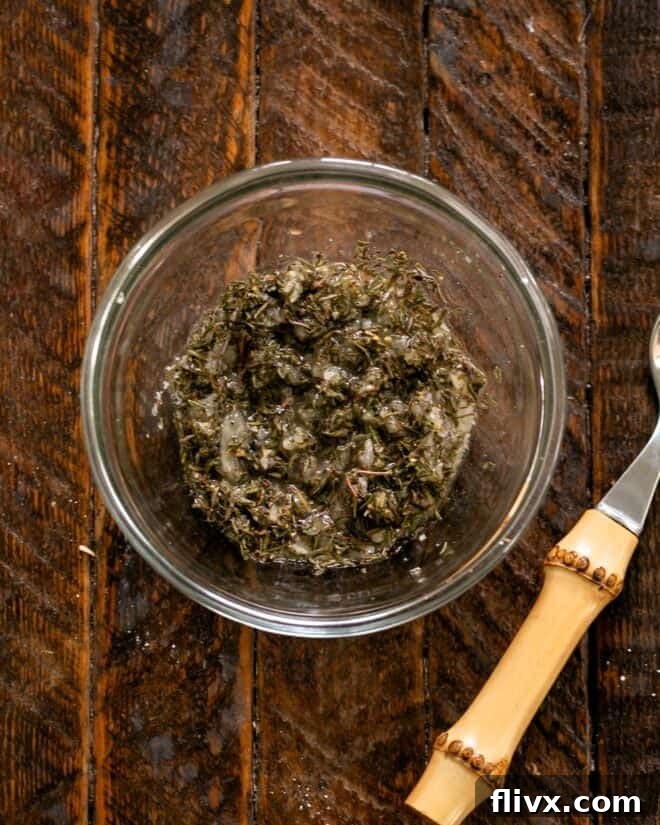A small glass bowl containing a vibrant, aromatic seasoning rub, a mixture of minced garlic, dried thyme, salt, pepper, and cider vinegar, ready to be applied to the chicken.