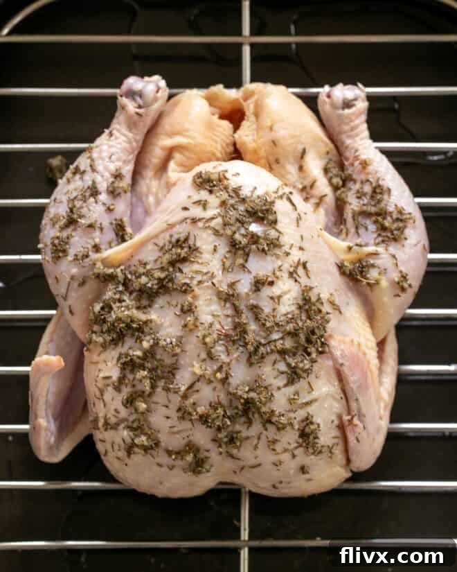 A whole raw chicken, meticulously covered with the rich garlic and thyme rub, with the mixture worked into every slash, ready for roasting.