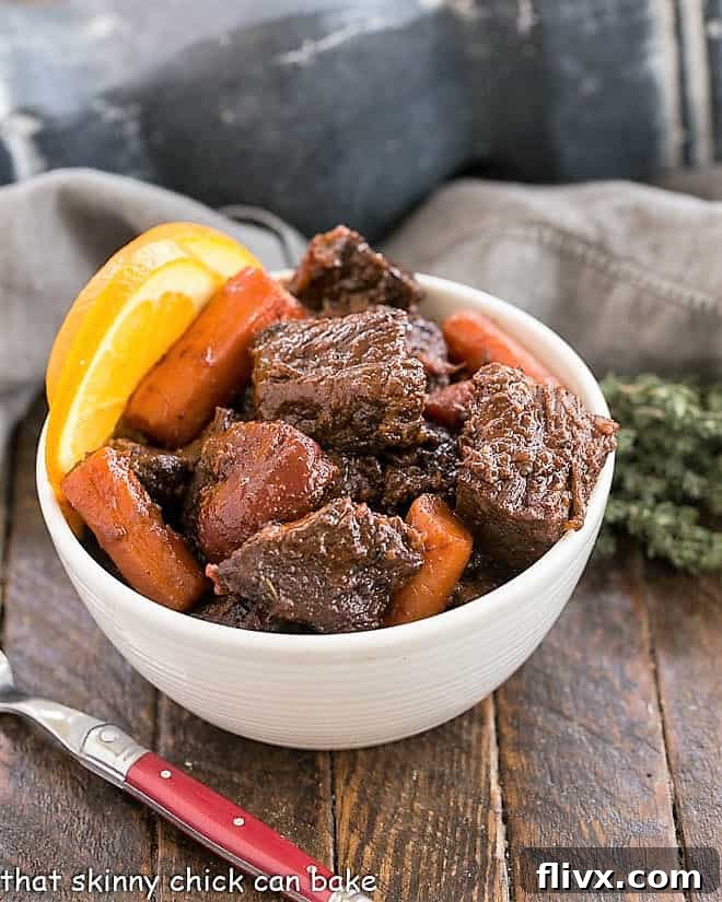 Beef Stew with carrots and orange slices in a white bowl with a red handled fork