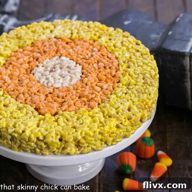 A stunning, uncut Candy Corn Rice Krispie Treat cake on a white cake stand, ready to be sliced into wedges.