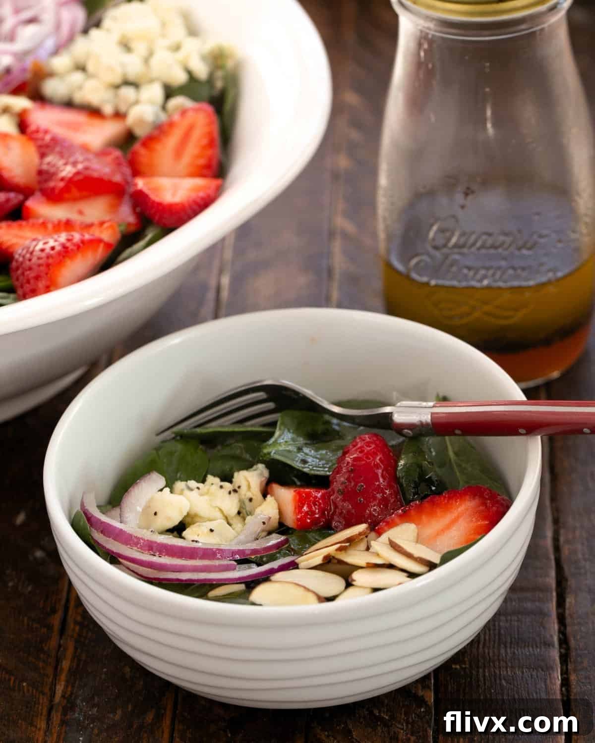 A beautifully presented small bowl of strawberry spinach salad, featuring vibrant greens, red strawberries, and creamy blue cheese, set against a larger serving bowl.