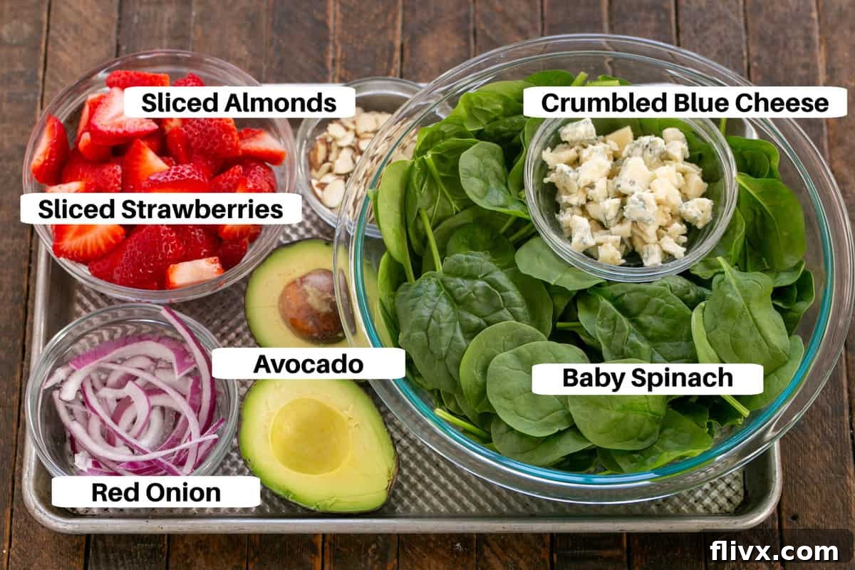 Various fresh ingredients for a spinach salad with strawberries and blue cheese, meticulously arranged on a sheet pan with labels.