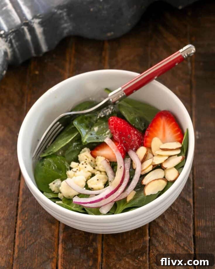 A delectable Strawberry Spinach Salad presented in a small bowl, garnished with blue cheese crumbles and a red-handled fork, ready to be enjoyed.